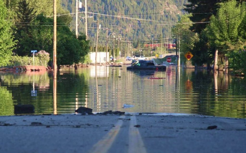 The centre-line of a road leads into a flooded street. In the distance, there's a pickup truck submerged up to its windows. 