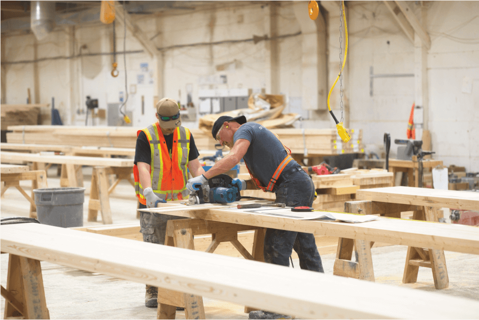 Two workers saw pieces of mass timber