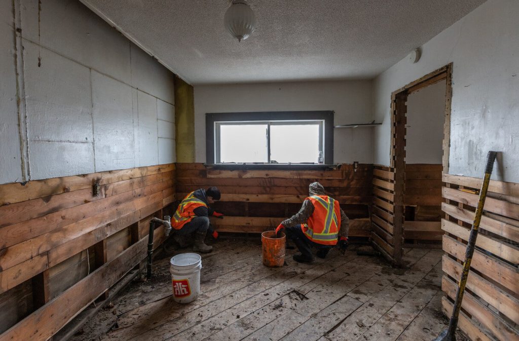 Two workers repairing a room that was damaged in a disaster.