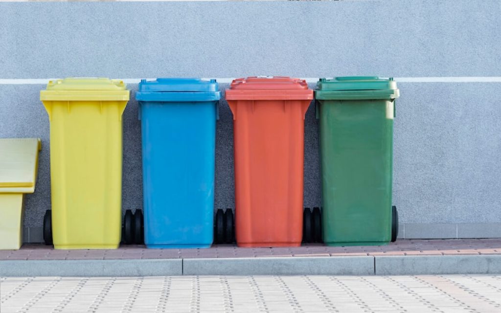 Colorful bins lined up against a gray wall represent waste we can divert from landfills, including paper, containers and food scraps.